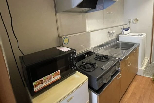 リゾートバイトの個室寮のキッチン。ガスコンロ、シンク、調理台が備え付けられ、奥には洗濯機とバスルームが見える、生活に必要な設備が揃った寮の画像。