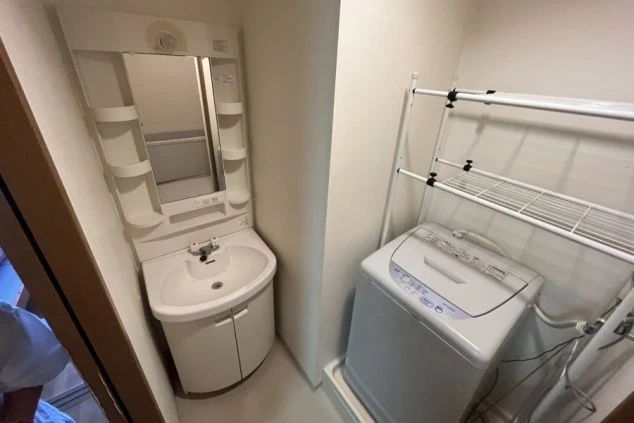 リゾートバイトの個室寮の洗面所。洗濯機と洗面台が設置され、鏡付きの収納棚もある、身だしなみや洗濯に便利な設備の寮の画像。