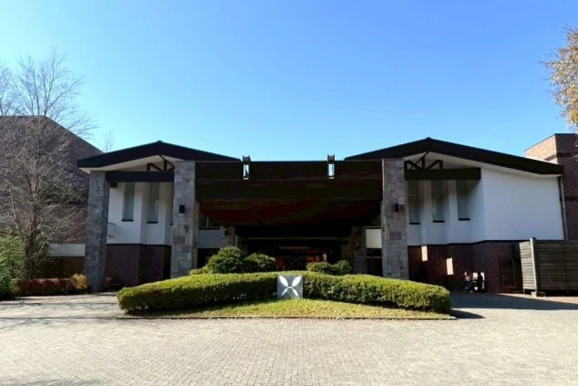 青空の下、軽井沢の自然に調和したモダンで広々としたホテルのエントランス。