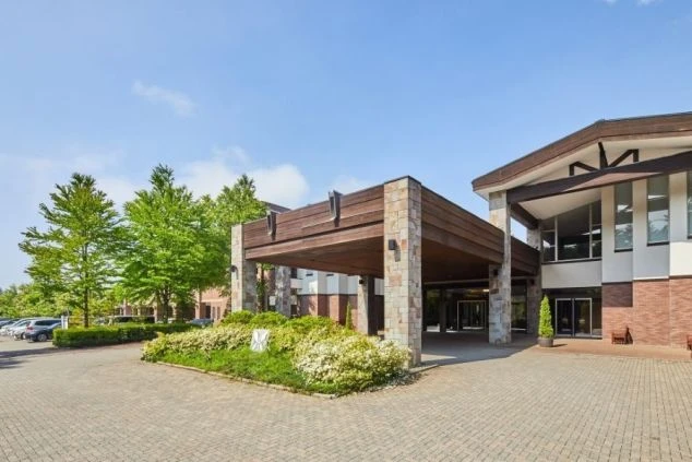 青空の下に建つ、石造りと木目調の外観が特徴的なホテルのエントランス。リゾートバイトで、ホテルのフロントやベルスタッフとしてお客様を迎える仕事に興味がある方に訴求する画像。