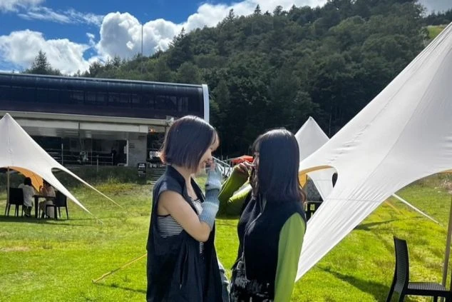 緑の芝生の上で笑顔で向かい合う2人の女性。背景にはテントやリフトが見え、リゾートバイトで出会った仲間とアウトドアや自然を楽しんでいる様子が伝わるワクトリスタッフが撮影したオリジナル画像。