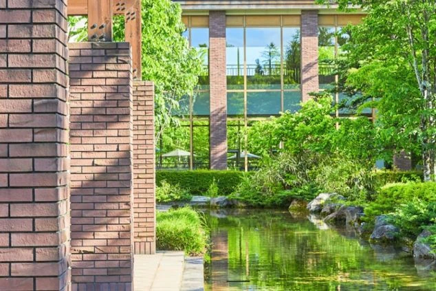 木とレンガ調の外壁が特徴的なホテルの外観。手前には池と緑豊かな庭園が広がり、リゾートバイトで自然に囲まれたホテルで働きたい方に訴求する画像。