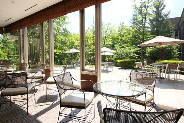 窓から緑豊かな庭園とテラス席が見えるカフェスペース。リゾートバイトでカフェやレストランのホール業務に携わり、開放的な空間で働きたい方に魅力的な画像。