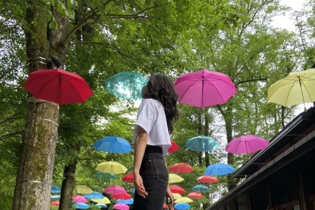 木々の間にカラフルな傘が吊るされた場所で、上を見上げる女性の後ろ姿。リゾートバイトの仕事の後に、おしゃれな観光スポットで思い出作りをしたい方に魅力的な画像。