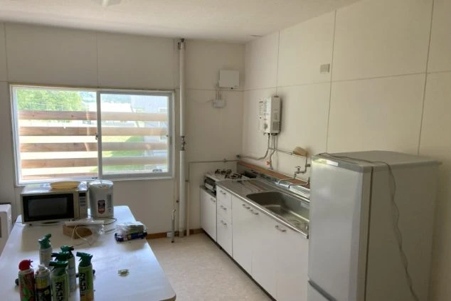 白いキャビネットとシンク、ガスコンロが備え付けられた共用キッチン。部屋には冷蔵庫、電子レンジ、そしてテーブルが置かれている。