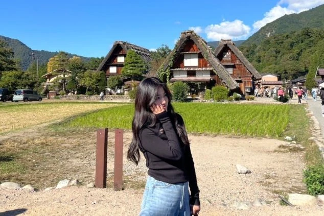 岐阜県白川郷のリゾートバイトの休日に観光する、合掌造りの家屋を背景にした女性の画像。