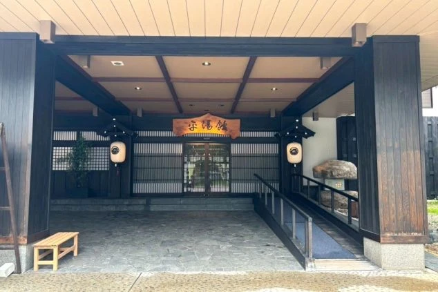 旅館の建物の玄関口の画像。茶色い看板に「宗湯館」という文字が書かれており、左右には提灯が飾られている画像。