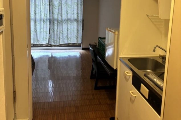 リゾートバイトの寮の部屋の全体像の画像。フローリングの床と窓があり、奥にはキッチンが見える。