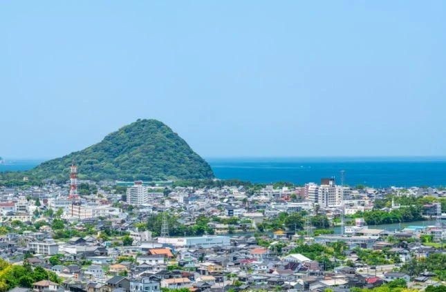 陸地の集落と、緑豊かな山、そして広がる海の景色。空は晴れている。