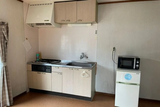 リゾートバイトの個室寮のキッチン。ガスコンロ、シンク、電子レンジ、冷蔵庫が備え付けられ、自炊ができる便利な設備の画像。