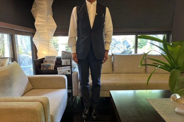 ホテルのラウンジで、白いシャツと紺色のベスト、パンツを着用した男性スタッフの制服。リゾートバイトでフロントやレストランの接客業務に興味がある方に訴求する画像。