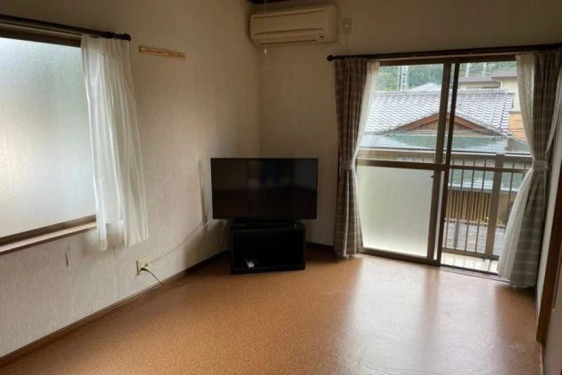 リゾートバイトの個室寮の室内。テレビとエアコンが備え付けられ、窓からは光が差し込む明るいリビングの画像。