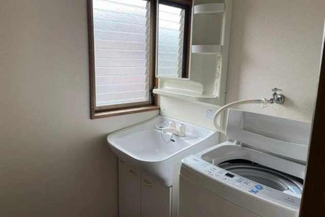 リゾートバイトの個室寮にある洗面所。洗面台の横には洗濯機が置かれており、身だしなみや洗濯に便利な設備の画像。