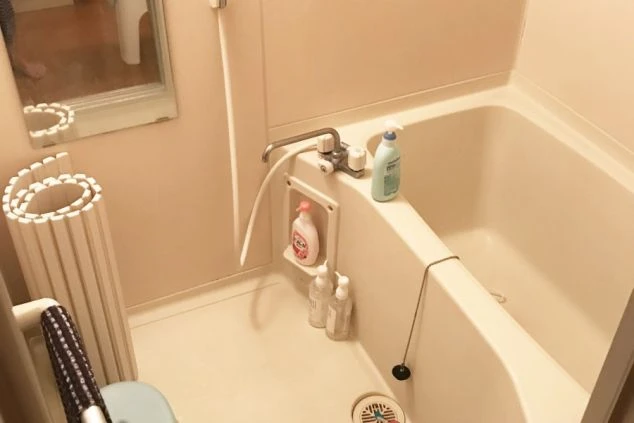 寮の浴室。浴槽と、鏡、シャワーが一体化したユニットバス。浴槽の縁にはシャンプー類が置かれている。