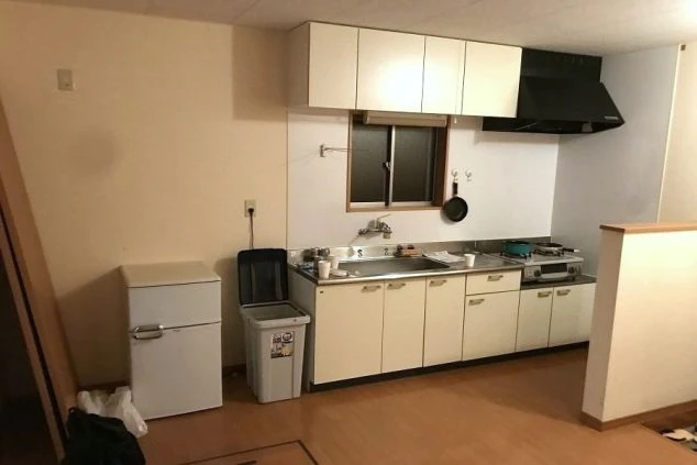 寮の共有キッチン。白いキャビネットとステンレスのシンク、二口ガスコンロがあり、小型の冷蔵庫とゴミ箱も備え付けられている。