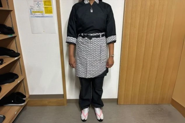 黒い上着とパンツ、白黒の模様が入ったエプロンを着用したスタッフの画像。足元は白足袋と草履を履いている。和食レストランや旅館でのリゾートバイトの仕事内容を表す、制服の画像。