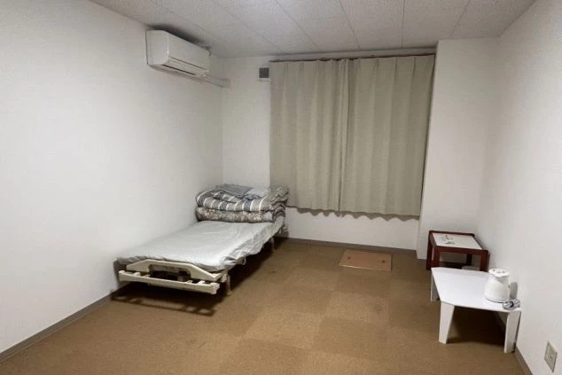 エアコンとテーブルが置かれたシンプルな寮の部屋。ベッドには布団が敷かれている。