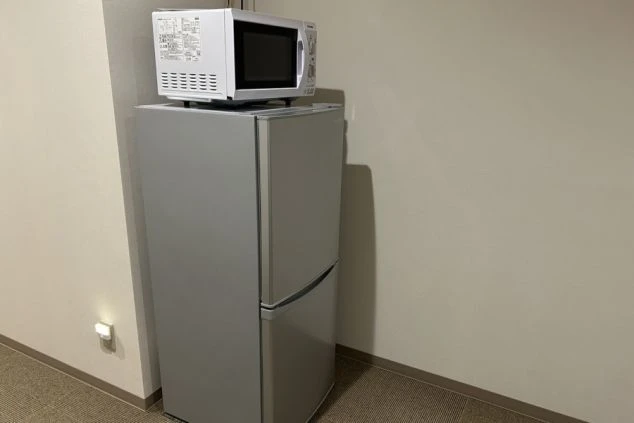 シルバーの冷蔵庫の上に電子レンジが置かれている。