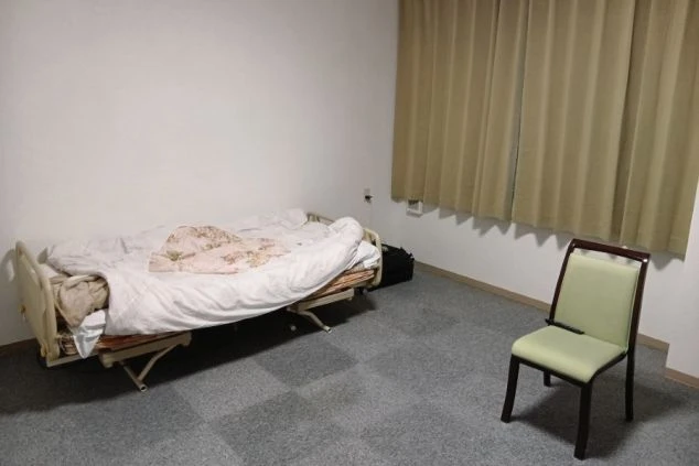 エアコンとテーブルが置かれたシンプルな寮の部屋。ベッドには布団が敷かれている。