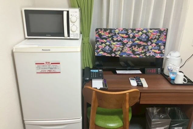冷蔵庫と電子レンジが置かれたデスク。デスクの上にはテレビ、電気ケトル、電話、リモコンが置かれている。
