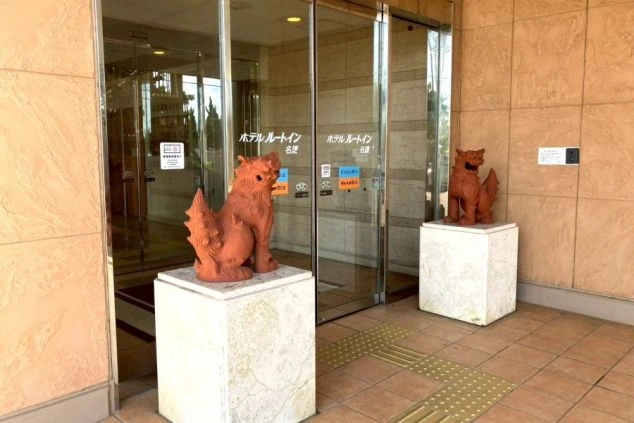 ワクトリの社員が出張で撮影した、リゾートバイトの寮の入り口の画像。ガラスの自動ドアの前に沖縄らしいシーサーの置物が二体あり、南国リゾートの雰囲気を醸し出している。