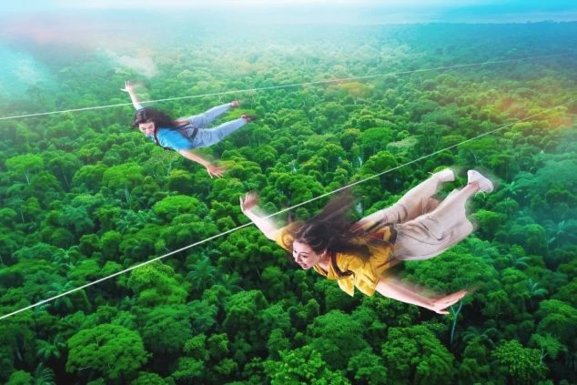 ジップラインでジャングルの上空を飛んでいる二人の女性。緑豊かな木々の上を滑空している。