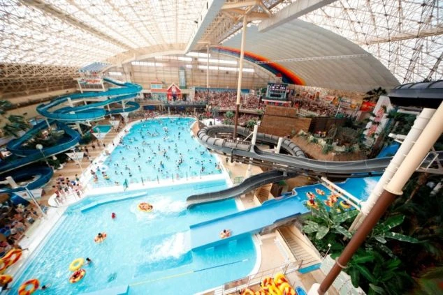 大勢の人で賑わう屋内プール。流れるプールやスライダーがあり、リゾートのような雰囲気が感じられる。