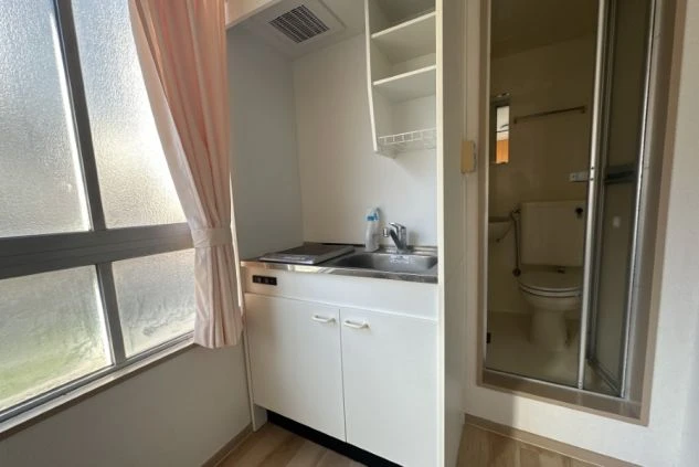 リゾートバイトの個室寮に完備されたミニキッチン。シンクとIHクッキングヒーターがあり、自炊で食費を節約できます。奥にはユニットバスも見えます。