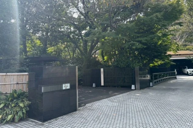 モダンなエントランス。黒い壁と門扉、竹垣が組み合わされ、敷石が敷かれた車寄せが見える。