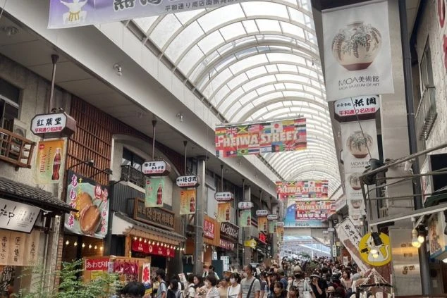 「平和通り」と書かれたアーケード商店街。たくさんの旗や看板が並び、多くの人で賑わっている。