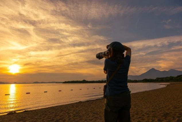 夕暮れの湖でカメラを構える人物。仕事終わりや休日に、絶景の写真を撮って楽しめる。