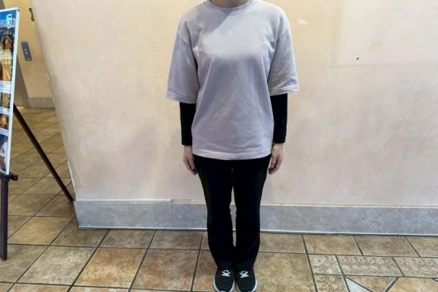 薄いベージュまたはグレーのTシャツと、黒い長袖インナー、黒いズボン、スニーカーを着用した人物