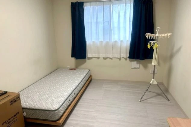 リゾートバイトの個室寮の室内。清潔感のあるフローリングで、ベッド、デスク、椅子、収納棚が備え付けられており、プライベートな時間を過ごすのに適しています。