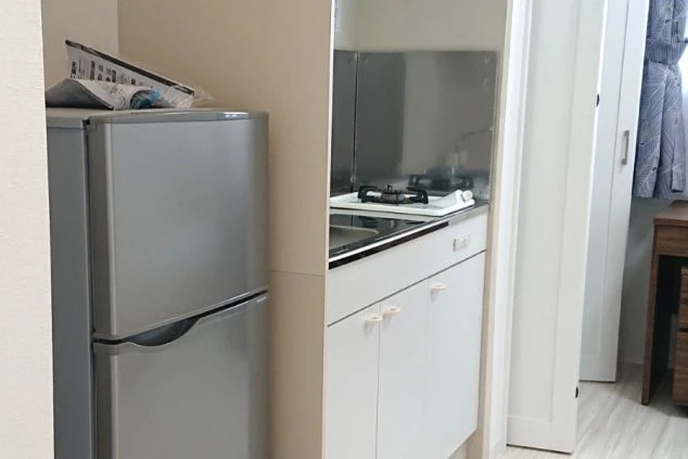 木製のデスクの上にある電子機器が写っています。デスクの左側には縦長の黒いモニター、中央には開いた状態のノートパソコンが置かれています。デスクの引き出しは茶色く、右下には椅子の背もたれの一部が見えます。