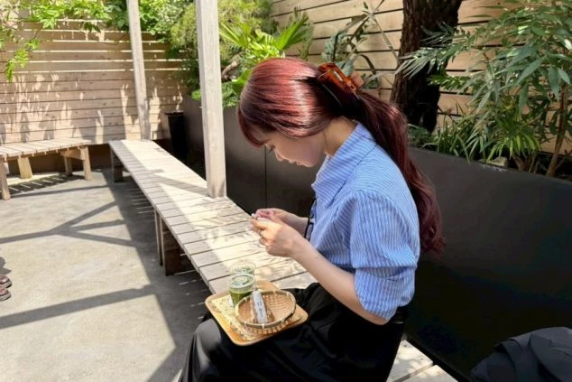 リゾートバイトの休憩時間や休日のイメージ画像。屋外のテラス席で抹茶と和菓子を楽しみながらスマートフォンを操作している女性。