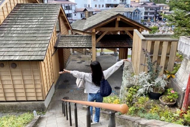  リゾートバイトの休日に観光を楽しむイメージ画像。群馬県草津温泉の湯畑周辺の階段で、両手を広げて街並みを眺めている女性の後ろ姿。