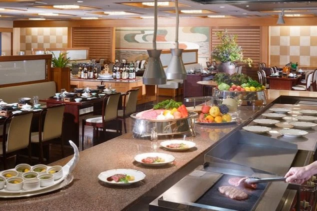 山と森に囲まれた、川向こうに建つベージュ色の水明館の建物群の外観。手前の建物には「北館」の文字が見える。