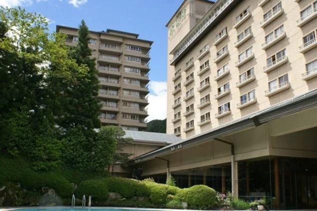 山と森に囲まれた、川向こうに建つベージュ色の水明館の建物群の外観。手前の建物には「北館」の文字が見える。