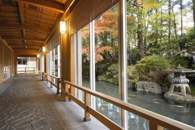 山と森に囲まれた、川向こうに建つベージュ色の水明館の建物群の外観。手前の建物には「北館」の文字が見える。