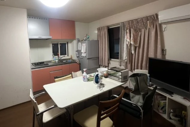 寮の共用リビング・キッチン。ピンク色のキャビネットのキッチン、冷蔵庫、テレビ、そしてテーブルの上にトースターやアイロンなどの家電が置かれている。