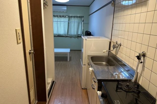リゾートバイトの寮の室内。玄関から部屋へと続く廊下に、キッチンと冷蔵庫が設置されている。