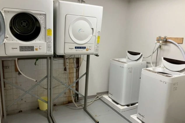 寮のランドリー。洗濯機と乾燥機が複数台並び、清潔な共用空間が映る。