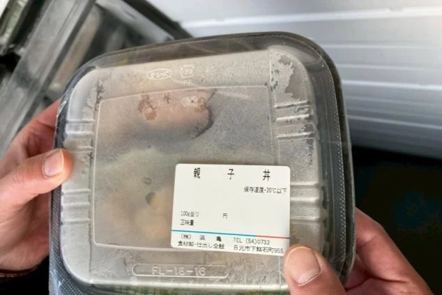 「親子丼」と書かれたラベルが貼られた冷凍のプラスチック容器を、両手で持っている様子。