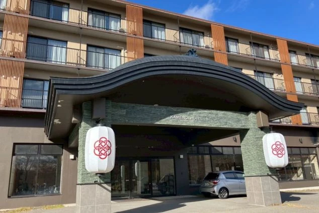 リゾートバイトの勤務先となるホテルの外観画像。大きな湾曲した黒い庇が特徴的で、左右に紋章入りの白い提灯が飾られている。