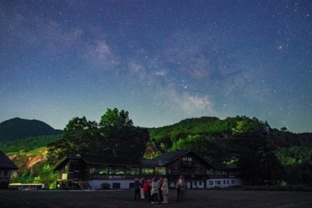 リゾートバイトの休日の観光イメージ画像。星が輝く夜空の下、ロッジ風の建物と木々の前で人々が景色を眺めている風景。