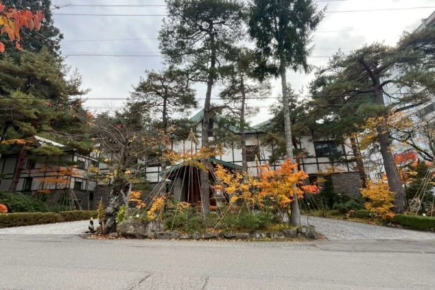 大きな石積みの柱と壁が特徴的で、木目調の玄関扉と、緑色の屋根の庇がある。上部は白壁に木の梁がデザインされた洋風の構造になっている。