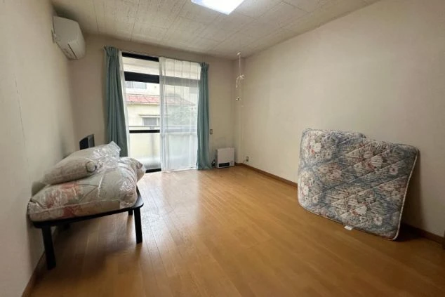 寮の個室。ベッドマット、テレビ、暖房器具、窓にカーテンが映る部屋の様子。