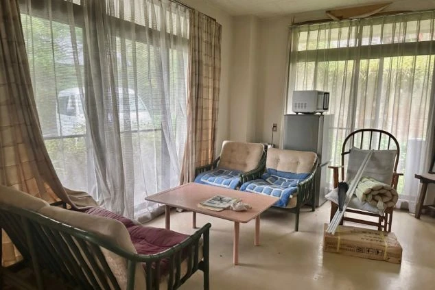 寮の共用リビング。ソファ、椅子、テーブル、レンジ、冷蔵庫、大きな窓が映る。