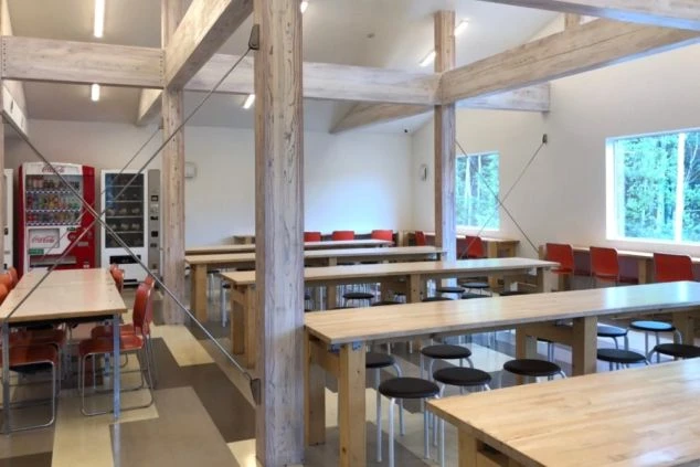 木製の大きなテーブルと椅子が多数並び、自動販売機も設置された広々とした空間が写っている画像。リゾートバイトの寮に併設された、スタッフが食事をしたり休憩したりできる食堂または休憩室のイメージ。