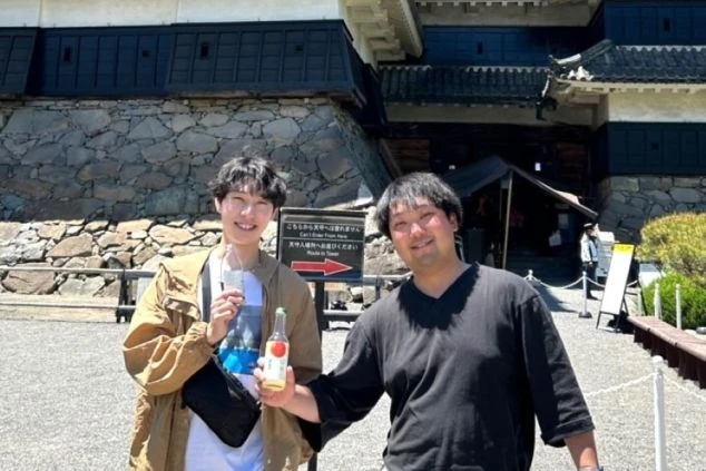 お城を背景に、飲み物を持った男性2人が笑顔で写っている画像。リゾートバイトの休日に歴史的な観光地を巡るイメージ。